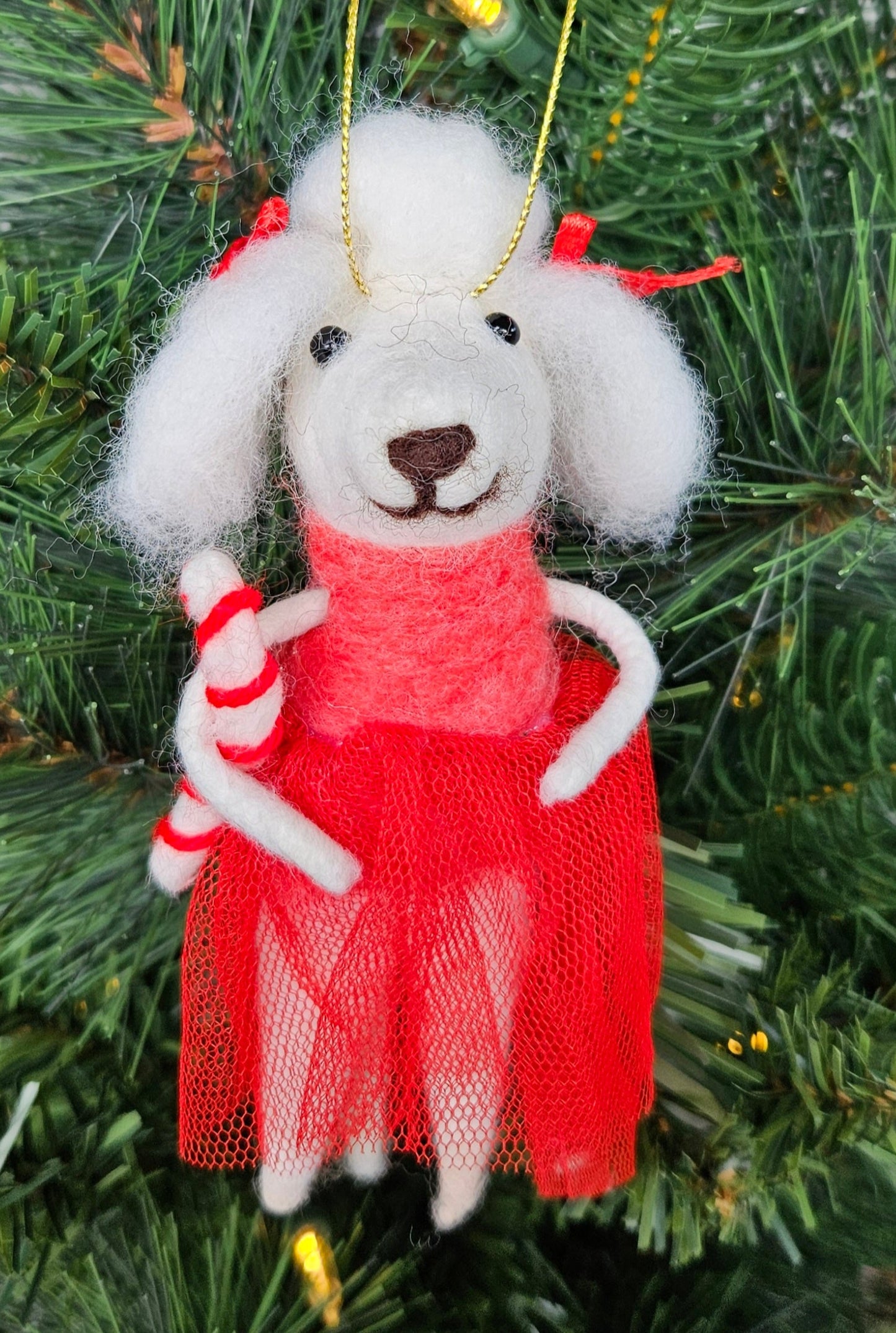 Decorative mouse ornament in a red dress hanging on a Christmas tree.