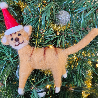 Felted animal ornament resembling a cat wearing a Santa hat on a Christmas tree.
