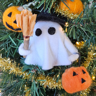 Halloween-themed ornament with a ghost, broom, and pumpkins on a decorated tree.