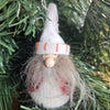 A grey bearded gnome Christmas decoration with a white hat with red stripes, placed among green tree branches.
