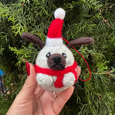 Small felted grey pug ornament with a red harness against a green foliage background