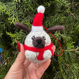 Small felted grey pug ornament with a red harness against a green foliage background