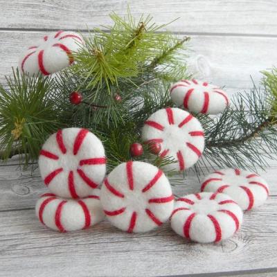 Felted Christmas decorations designed to look like peppermints, red and white striped, displayed on a wooden surface with greenery in the background.